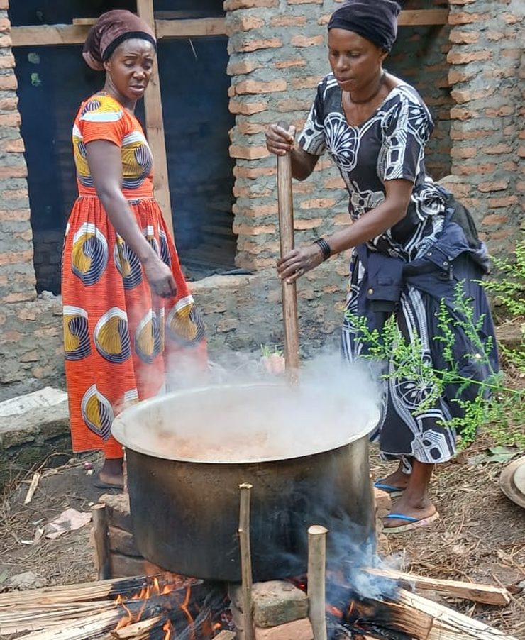 Two women cooking in a large pot over an open fire